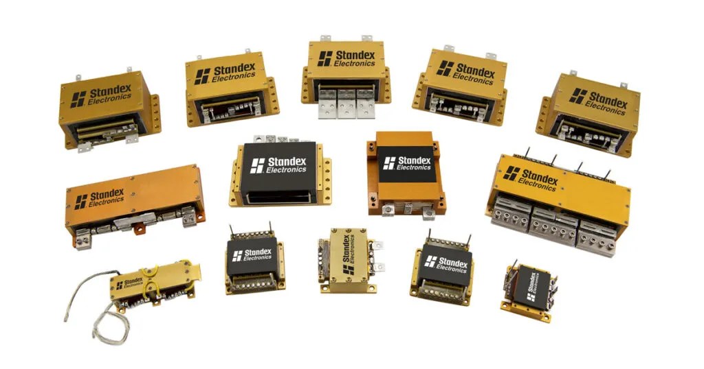 Thirteen variously sized and shaped yellow and black Standex Electronics components, including relays, connectors, and a power inductor, are arranged on a white background. by Standex Edge