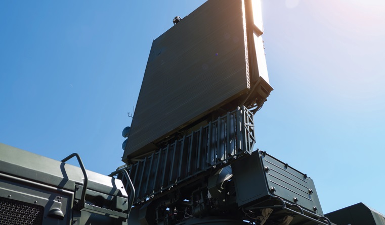 A large military radar system mounted on a vehicle stands against a clear blue sky, with sunlight shining from the top right corner. The system incorporates advanced components like a high frequency transformer for enhanced performance. by Standex Edge