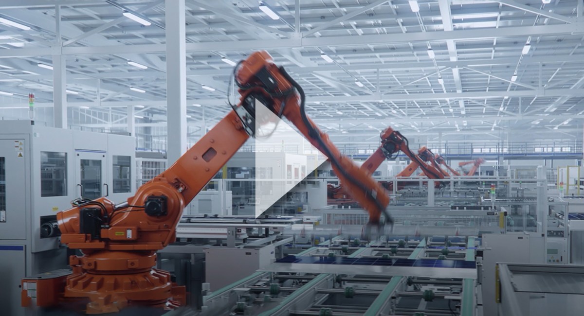 Orange robotic arms, part of advanced automation equipment, operate on an automated assembly line inside a modern, brightly lit factory with white walls and ceiling. by Standex Edge