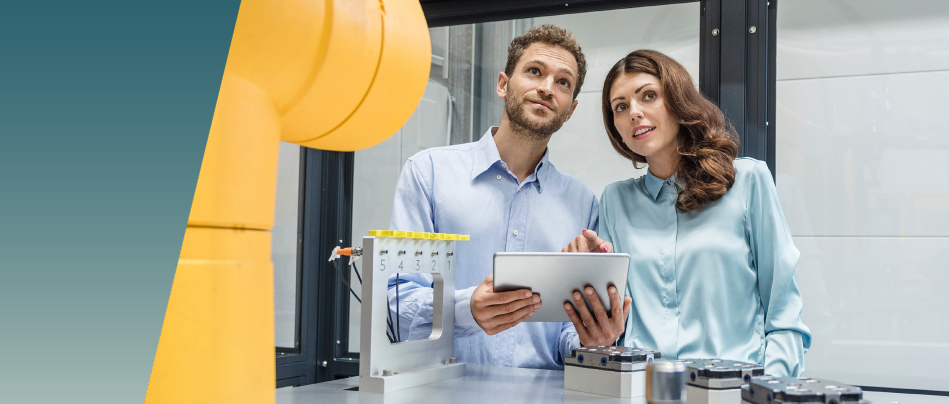 Two people stand in a high-tech lab, discussing a robotic arm. One holds a tablet as they analyze clearance and creepage data critical to the machinery’s safe operation. by Standex Edge