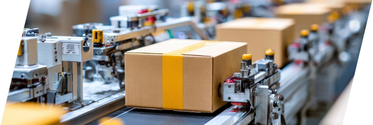 Cardboard boxes with yellow tape move along a conveyor belt in an automated packaging facility, where precise clearance and creepage distances are maintained among the industrial machinery and equipment. by Standex Edge