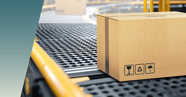 A cardboard box with handling symbols sits on a conveyor belt in a warehouse or packaging facility, where careful attention is given to clearance and creepage distances to ensure safe and efficient packaging processes. by Standex Edge